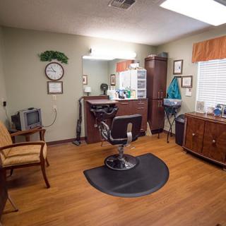 Interior of a barbershop with a central chair facing a mirror and various furniture pieces.