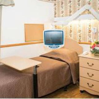 A hospital room with a bed, overbed table, television, and flower arrangement.
