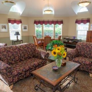 A cozy living room with floral sofas and a coffee table adorned with a sunflower arrangement, brightened by natural light through the windows.