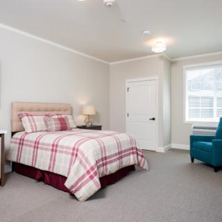 A cozy bedroom featuring a bed with plaid bedding, an armchair, and a window allowing natural light.