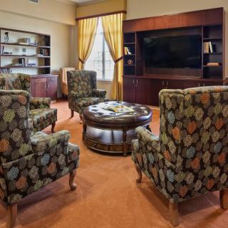 A cozy living room with patterned armchairs, a central coffee table, and built-in bookshelves framing a large television.