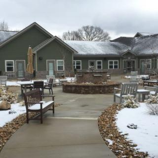 A snowy courtyard with benches and chairs outside a building on an overcast day.