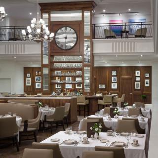 A sophisticated restaurant interior featuring a large clock, elegant chandelier, and neatly arranged dining tables.