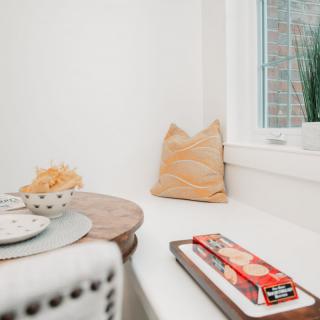 A cozy nook with a round table, snacks on a plate, and a window seat with cushions.
