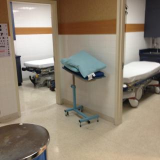 A hospital hallway with empty medical beds and a small table with linens.