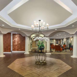 A luxurious hotel lobby featuring a central chandelier, elegant columns, and stylish decor.