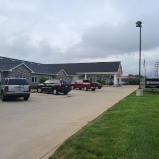A view of a commercial building with a parking lot filled with various vehicles under a cloudy sky.