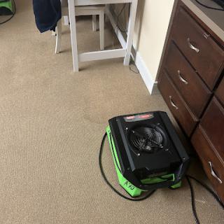A carpet dryer positioned on the floor near some furniture.