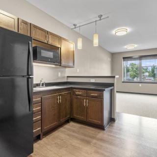A modern apartment kitchen with wood cabinets and black appliances.