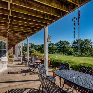 A spacious patio with metal tables and chairs overlooks a lush garden on a sunny day.