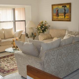A cozy living room with comfortable sofas, a vibrant carpet, and tasteful decor, including a painting and flower arrangement.