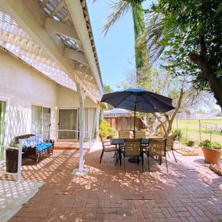 A sunny outdoor patio with garden furniture and an umbrella, surrounded by lush trees.