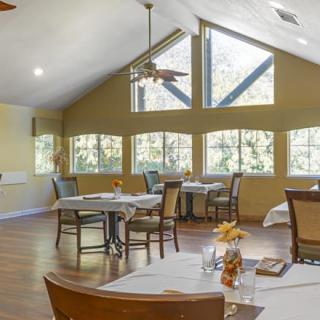 A bright dining room with tables and chairs, featuring large windows and high ceilings.