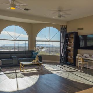 A spacious living room with large arched windows allowing ample natural light, featuring a comfortable sofa, elegant coffee table, wall-mounted TV, and a neatly organized bookshelf.