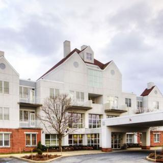 A residential building with a prominent white facade and red brick accents under a cloudy sky.