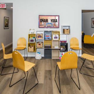 A minimalist yoga studio waiting area with yellow chairs and a central bookshelf on a wooden floor.