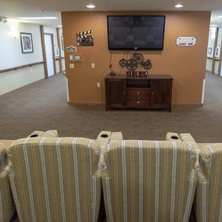 A cozy seating area with striped chairs facing a wall-mounted television in a well-lit room.