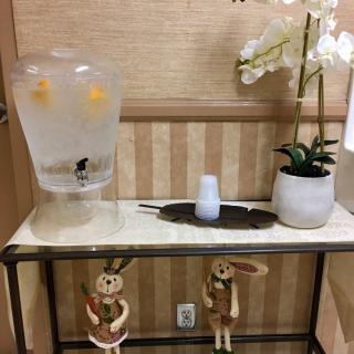 A decorative table with a lemon-infused water dispenser, orchids, and two hanging dolls.