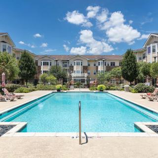A sunny day view of a swimming pool surrounded by an apartment complex and landscaped gardens.