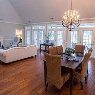 A spacious open-plan living and dining room with hardwood floors, featuring a prominent chandelier and French doors leading outside.