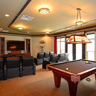 A cozy entertainment room featuring a pool table, home theater setup, and comfortable seating.