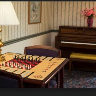 A cozy room featuring a chessboard on a table, with a lamp and piano in the background.