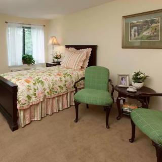 A cozy bedroom with floral bedspread, green armchairs, and soft lighting.