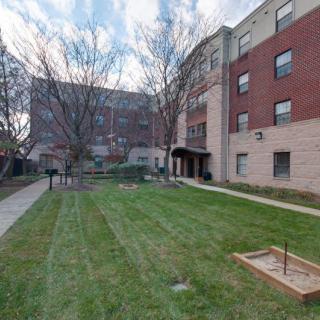 A view of an apartment building with a manicured lawn and trees lining the walkway.