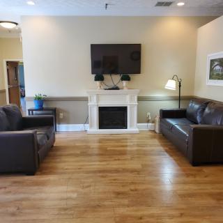 A cozy living room with two sofas, a TV mounted above a fireplace, and wooden floors.