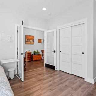 A bright interior space with double doors leading from a bedroom to a living room, featuring hardwood floors and white walls.