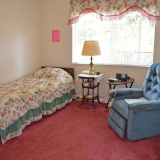 A cozy bedroom with a floral bedspread, blue armchair, and a lamp beside the window.