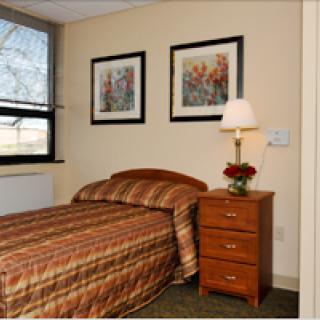 A cozy bedroom featuring a single bed, a nightstand with a lamp, and framed artwork on the walls.