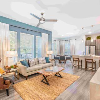 A modern open-floor living area featuring a cozy sofa, stylish coffee table, and a kitchen with a large island and bar stools.