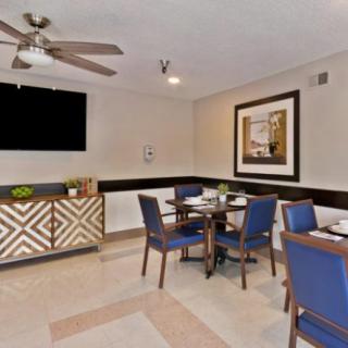 A modern dining room with a table and blue chairs, featuring artwork on the wall and a ceiling fan.