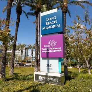 A sign for Long Beach Memorial, a medical facility, set against a background of trees and clear blue sky.