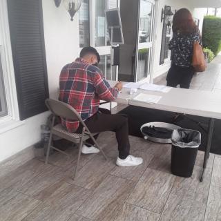 A person sits at a table outdoors, writing in a notebook.