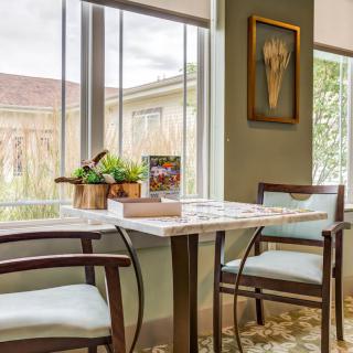 A cozy dining area with a marble table, wooden chairs, and natural light streaming through large windows.