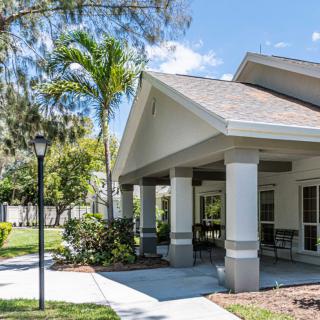 A pleasant residential house with a covered patio and surrounding palm trees on a sunny day.