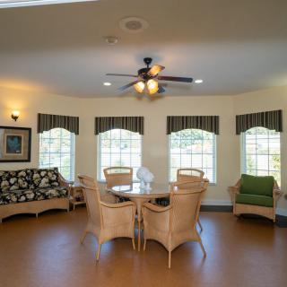 A cozy living room with wicker furniture, a ceiling fan, and large windows allowing natural light to fill the space.