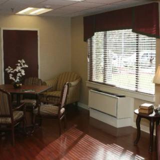A cozy living room with a table and chairs, featuring large windows with blinds and curtains.