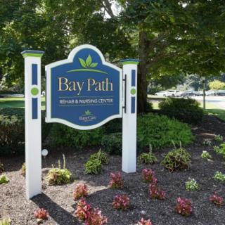 A decorative sign for Bay Path in a landscaped garden setting.