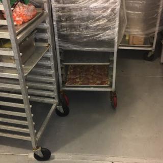 A view of a commercial kitchen with metal racks and an empty cart.