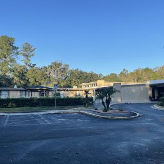 A quiet parking lot surrounded by buildings and trees under a clear blue sky.
