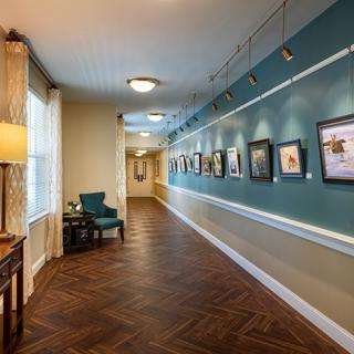 A modern hallway with a gallery of paintings displayed along the wall, featuring wood flooring and elegant lighting.