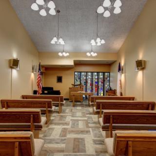 An interior view of a small church with wooden pews and stained glass windows.