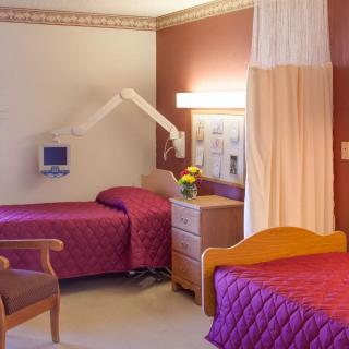 A hospital room with two patient beds, medical equipment, and a privacy curtain.