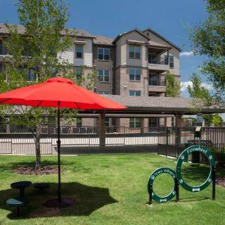 An outdoor space in an apartment complex featuring a lawn with a red umbrella and pet play equipment.