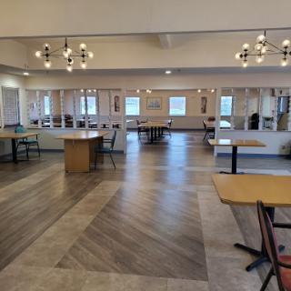 A spacious and well-lit dining area featuring simple wooden tables and chairs, designed for gatherings.