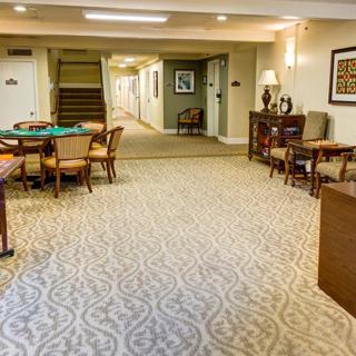 A cozy lobby area with carpeted flooring, tables, and chairs leading to a hallway.