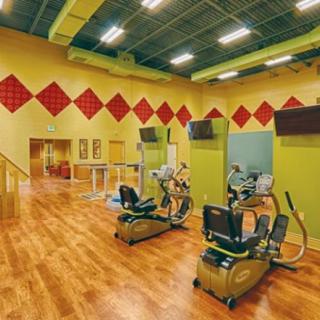 A fitness center with exercise bikes and treadmills, featuring wooden flooring and overhead televisions.
